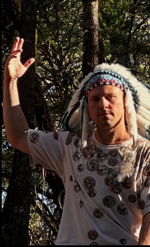 Daniel Dabek outdoors among trees, raising one hand.